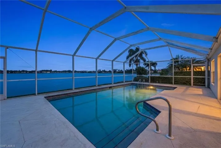 Swimming pool with glass enclosure, a sunroom, a water view, and a patio