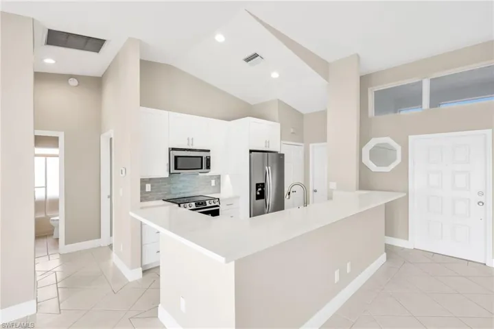 Kitchen with appliances with stainless steel finishes, high vaulted ceiling, decorative backsplash, white cabinetry, and light tile patterned floors