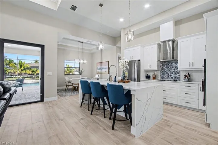 Kitchen featuring hanging light fixtures, a kitchen breakfast bar, light stone counters, a center island with sink, and white cabinetry