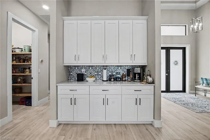 Coffee Bar area with white cabinetry, backsplash, light wood-type flooring, hanging light fixtures, and a towering ceiling