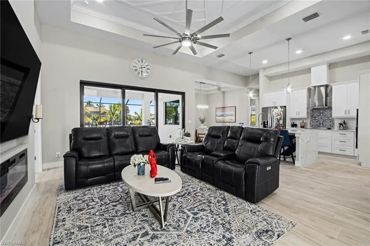 Living area featuring a high ceiling, light wood finished floors, a ceiling fan, ornamental molding, and a glass covered fireplace