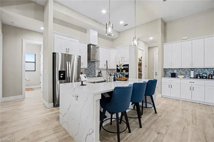 Kitchen with decorative backsplash, white cabinets, light stone counters, stainless steel fridge with ice dispenser, and light wood-type flooring