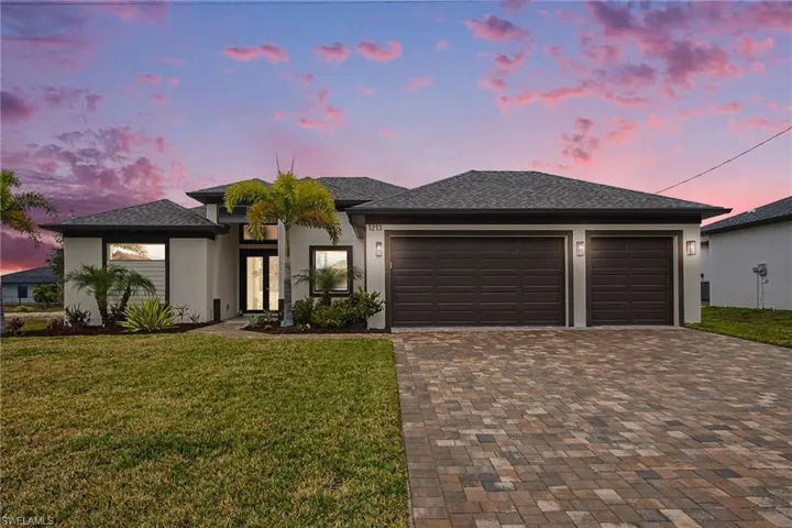 View of front facade with stucco siding, a lawn, driveway, a garage, and roof with shingles