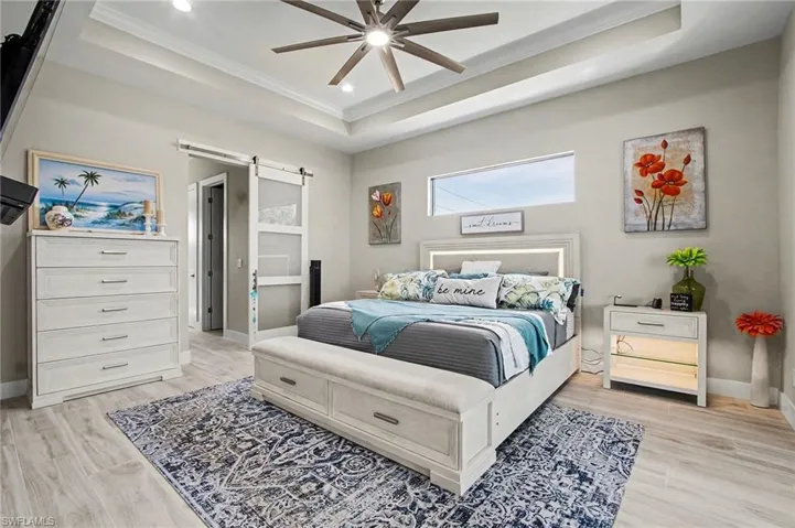 Master Bedroom featuring a barn door, light wood finished floors, recessed lighting, a raised ceiling, and ornamental molding