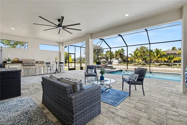 View of patio featuring exterior kitchen, a sunroom, ceiling fan, glass enclosure, and an outdoor pool