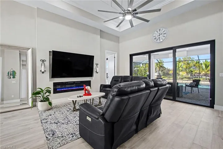Living area with light wood finished floors, a high ceiling, a glass covered fireplace, a ceiling fan, and crown molding