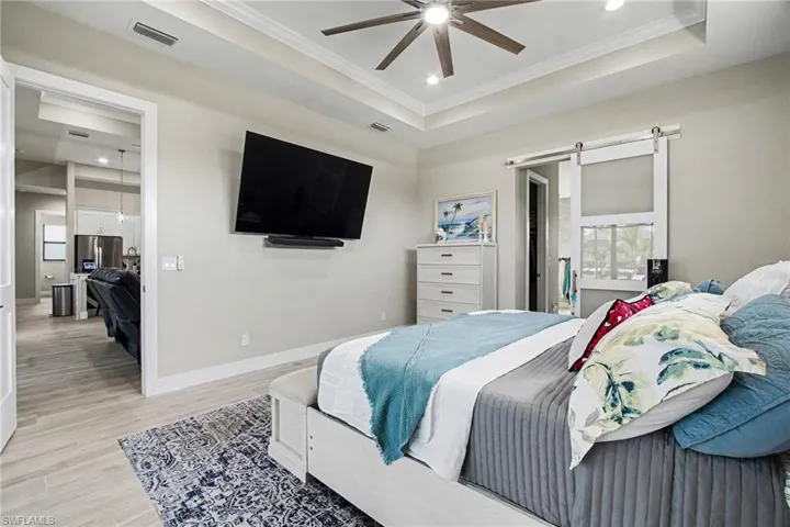 Master Bedroom featuring a barn door, light wood finished floors, recessed lighting, a raised ceiling, and ornamental molding