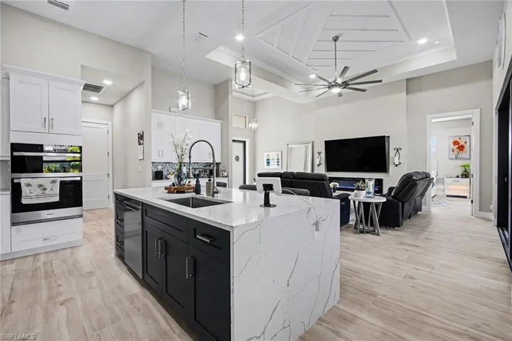 Kitchen with white cabinets, dark cabinets, light stone counters, hanging light fixtures, and light wood-type flooring