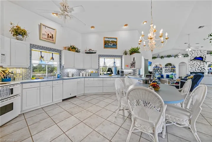 Kitchen featuring white cabinetry, pendant lighting, white appliances, ceiling fan with notable chandelier, and backsplash