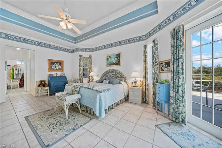 Tiled bedroom featuring ornamental molding, a tray ceiling, multiple windows, and access to outside