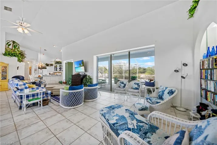 Living room with tile patterned flooring, ceiling fan with notable chandelier, and high vaulted ceiling
