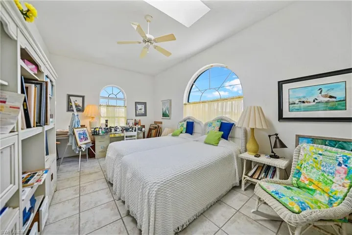 Tiled bedroom featuring ceiling fan and vaulted ceiling with skylight