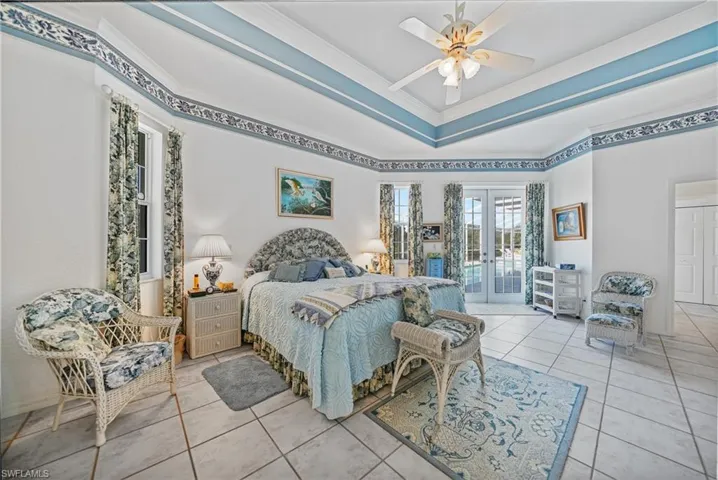 Tiled bedroom featuring access to outside, ceiling fan, a raised ceiling, crown molding, and french doors