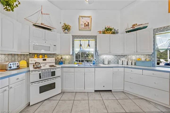 Kitchen featuring white cabinetry, white appliances, decorative backsplash, and a wealth of natural light