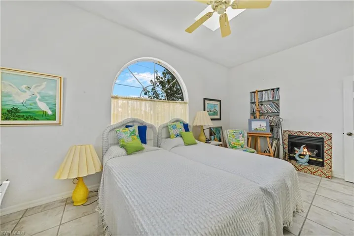 Bedroom featuring light tile patterned flooring, lofted ceiling, ceiling fan, and a fireplace