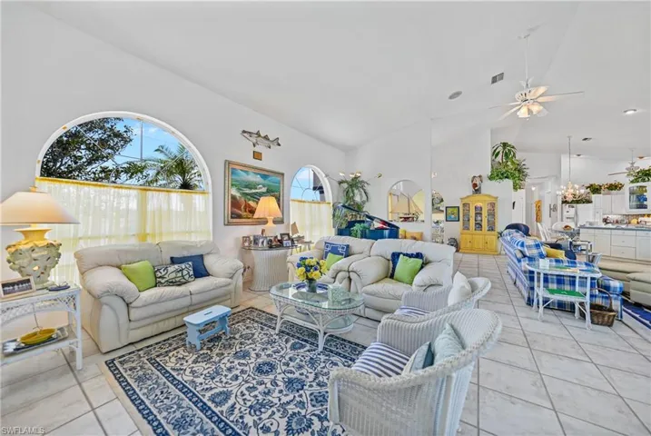 Living room with light tile patterned flooring, ceiling fan with notable chandelier, and high vaulted ceiling