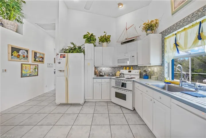 Kitchen with light tile patterned flooring, white cabinetry, sink, backsplash, and white appliances