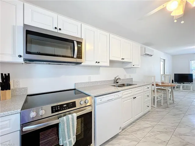 Kitchen with sink, ceiling fan, white cabinetry, appliances with stainless steel finishes, and a wall mounted air conditioner