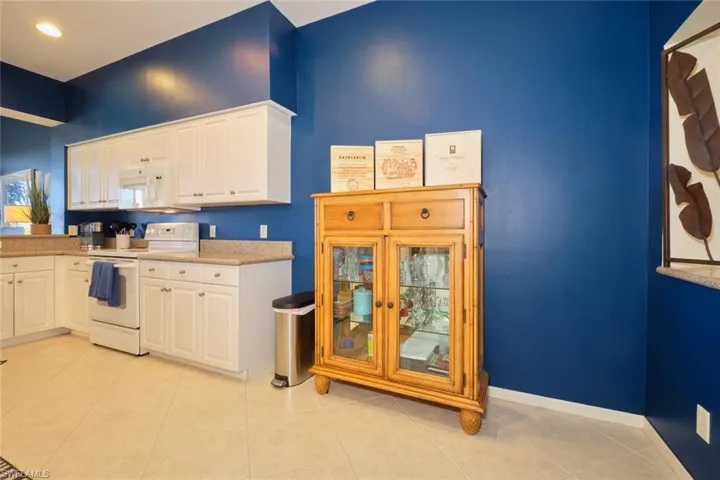 Kitchen with white appliances, white cabinetry, and light tile patterned flooring