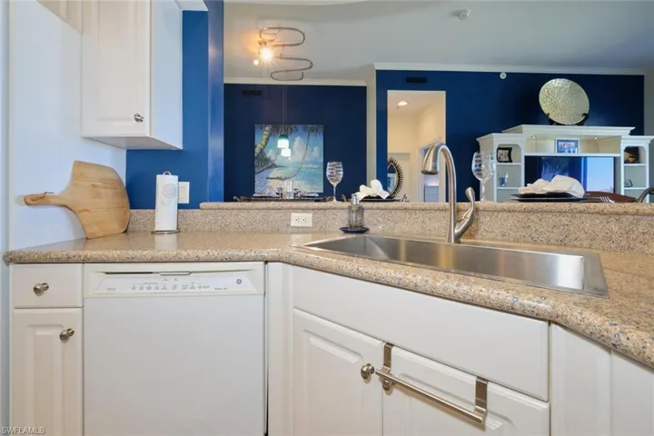 Kitchen with white dishwasher, sink, light stone countertops, ornamental molding, and white cabinetry