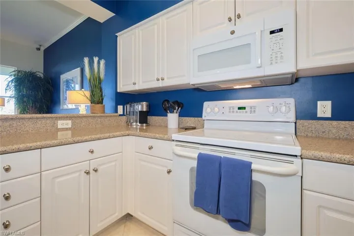 Kitchen featuring white appliances, white cabinets, light stone countertops, ornamental molding, and light tile patterned floors