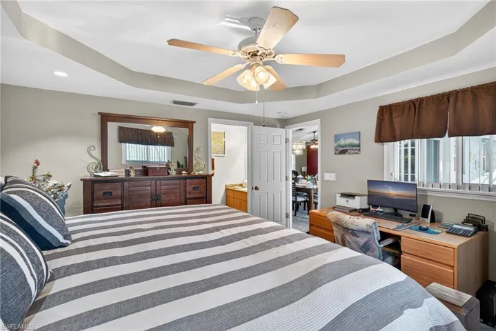 Bedroom featuring a raised ceiling, a ceiling fan, ensuite bath, and recessed lighting