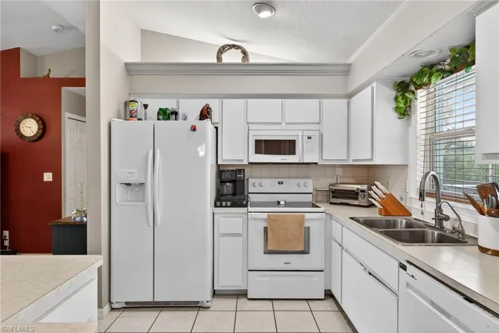 Kitchen with white appliances, light countertops, white cabinetry, and backsplash