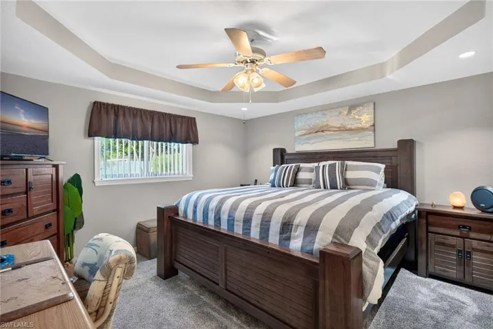 Carpeted bedroom with a ceiling fan and a tray ceiling