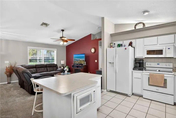 Kitchen featuring white appliances, white cabinetry, open floor plan, vaulted ceiling, and light countertops