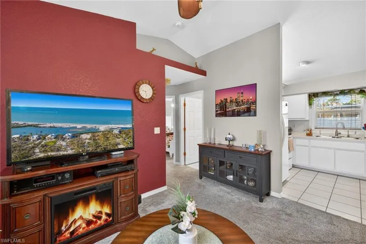 Living room with light carpet, lofted ceiling, a lit fireplace, light tile patterned floors, and ceiling fan
