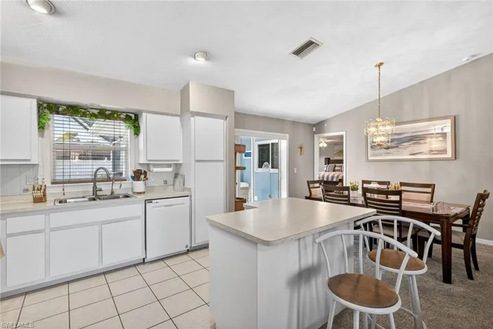 Kitchen with white cabinets, white dishwasher, a breakfast bar area, light countertops, and light tile patterned floors