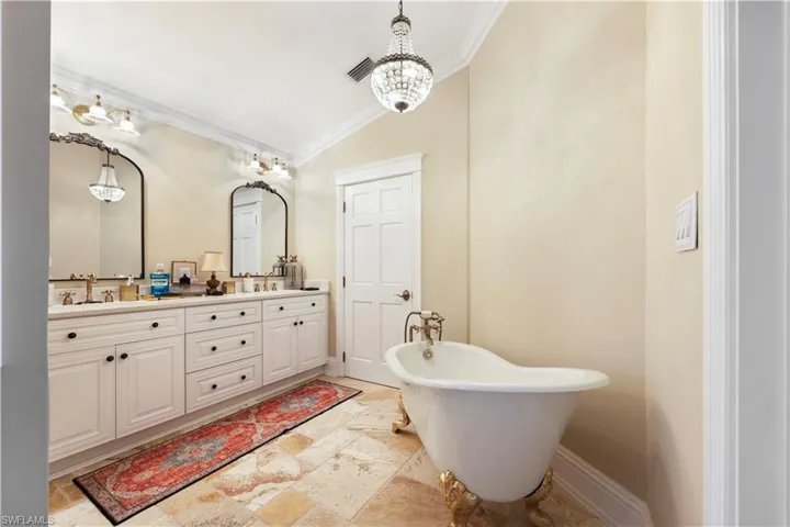 Full bathroom with lofted ceiling, double vanity, a freestanding tub, crown molding, and suspended lighting