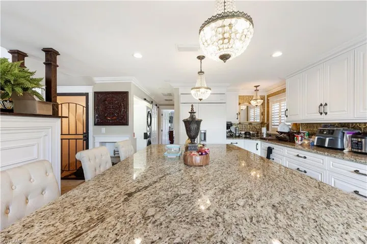 Kitchen with light stone counters, tasteful backsplash, white cabinets, suspended lighting, and a barn door