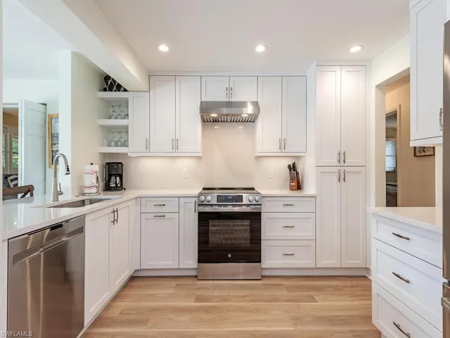 Kitchen featuring open shelves, under cabinet range hood, white cabinets, a sink, and stainless steel appliances