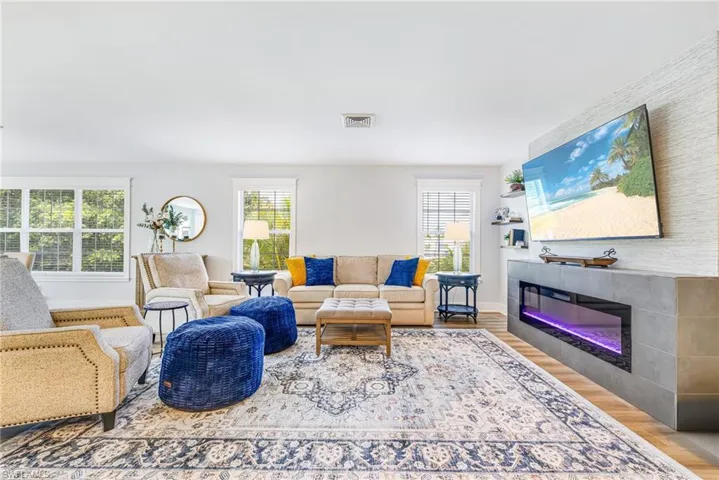 Spacious living area featuring light-tone wood-finish flooring, multiple windows providing natural illumination, and a contemporary linear fireplace