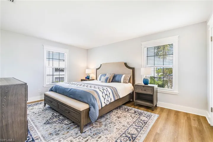 Bright bedroom featuring two windows with white trim, wood-finish flooring, and white baseboards