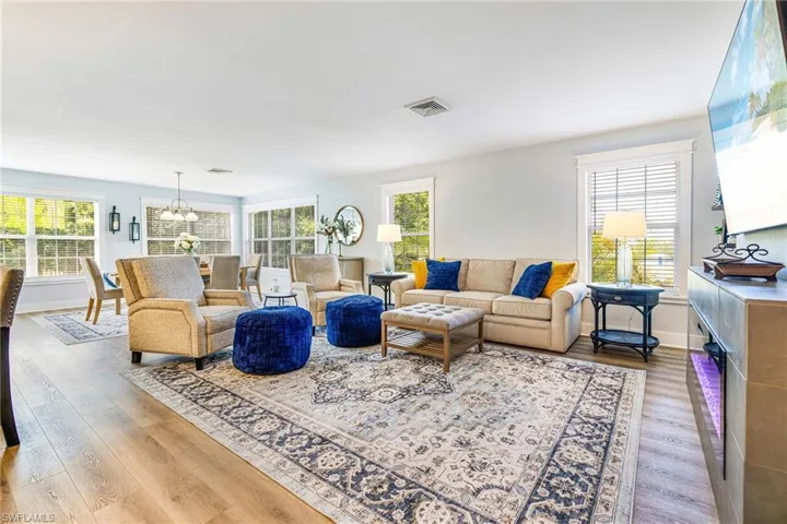 Expansive living space featuring wood-finish flooring, multiple windows with white trim, and a built-in media console with ambient lighting