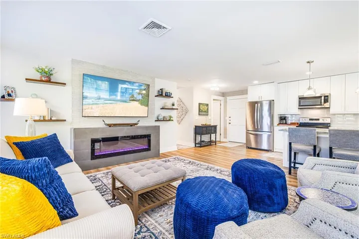 Open-concept living space featuring wood-finish flooring, a contemporary electric fireplace with a tiled surround, and white walls