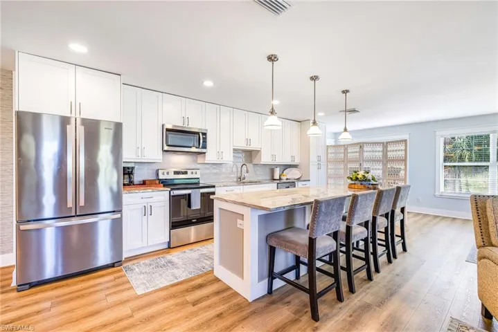 Modern kitchen featuring a breakfast bar island, stainless steel appliances, white cabinetry, wood-finish flooring, and pendant lighting