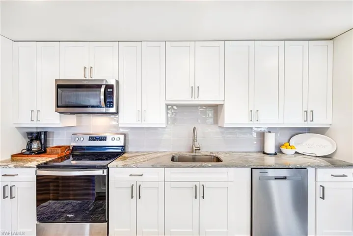 Kitchen featuring white shaker-style cabinetry, stainless steel appliances, a tiled backsplash, a stainless steel sink with a gooseneck faucet, and stone countertops