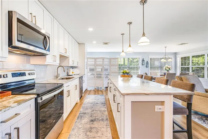 Open-concept kitchen featuring white cabinetry, stainless steel appliances, a large center island with seating, and wood-finish flooring