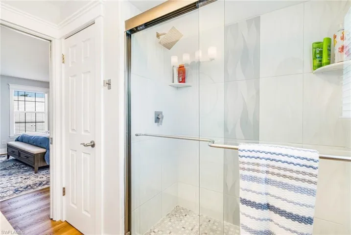Glass-enclosed shower with a rainfall showerhead, integrated shelving, and pebble tile flooring