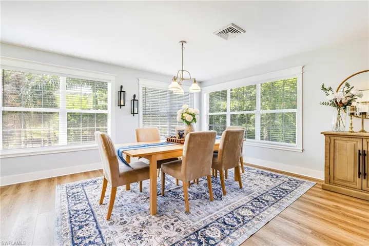 Bright room featuring multiple windows with horizontal blinds, wood-finish flooring, and a ceiling-mounted light fixture