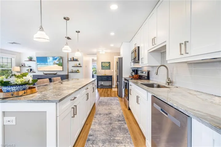 Contemporary kitchen featuring an expansive center island with stone countertop, white shaker cabinetry, stainless steel appliances, and wood-finish flooring