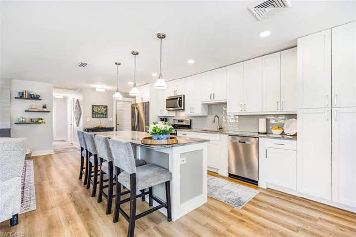 Kitchen featuring an expansive island with seating, white shaker-style cabinetry, stainless steel appliances, wood-finish flooring, and pendant lighting