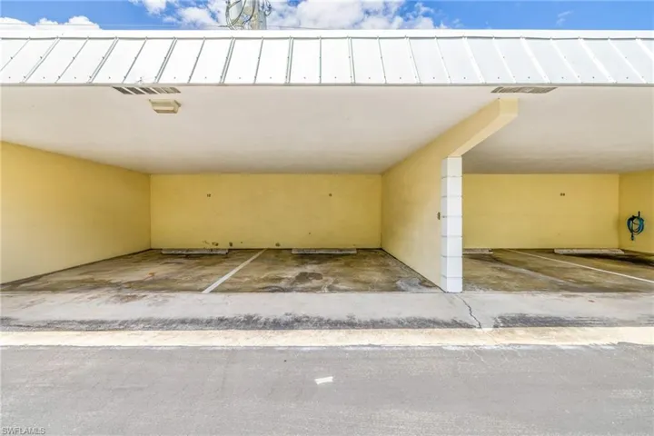 Covered parking structure featuring a metal panel roof, two designated parking spaces with concrete wheel stops, and a hose reel mounted on the wall