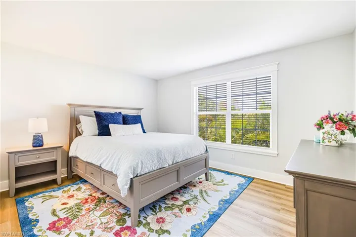Bedroom featuring light-tone wood-finish flooring, white walls, and a large window with white blinds and trim