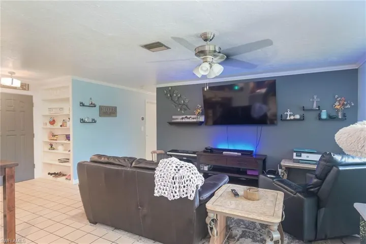 Living room featuring light tile patterned floors, ceiling fan, a textured ceiling, built in features, and crown molding