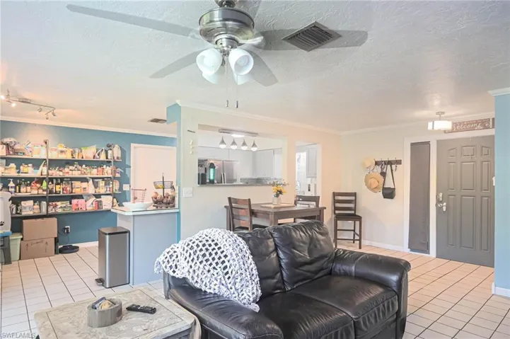Tiled living room with ceiling fan, ornamental molding, and a textured ceiling