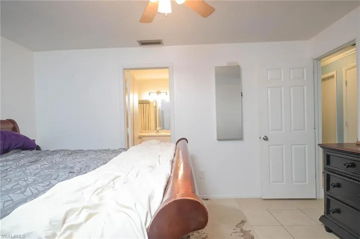Bedroom featuring ensuite bath, light tile patterned floors, and ceiling fan